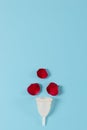 Menstrual cup and red rose petal on a blue background.