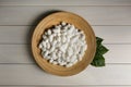 Silk cocoons with plate and leaves on white wooden table, flat lay