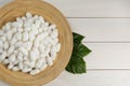 Silk cocoons with plate and leaves on white wooden table, flat lay. Space for text