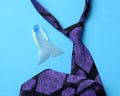Silk purple mens tie and blue ribbon folded in a loop on blue background