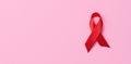 A silk red ribbon in the form of a bow on a pink background, a symbol of the fight against AIDS and a sign of solidarity and
