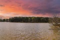 A silky brown still lake surrounded by lush green trees and powerful red storm clouds reflecting off the water  at sunset Royalty Free Stock Photo