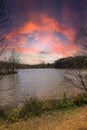 A silky brown still lake surrounded by lush green trees and red sky and powerful clouds reflecting off the water at sunset Royalty Free Stock Photo