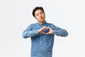 Silly handsome asian young guy in blue shirt confessing love, express sympathy, blogger grateful for followers, showing