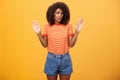 Silly insecure and sad dark-skinned female model in trendy striped t-shirt and shorts raising arms in surrender frowning