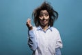 Silly looking crazy chemist with dirty face and messy hair looking at camera on blue background.