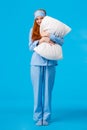 Silly romantic and cute, gentle young redhead coquettish woman in pyjama and sleep mask, hugging pillow peeking at