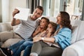 Silly selfies are the best selfies. a young family of four taking selfies together with a digital tablet on the sofa at Royalty Free Stock Photo