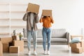 Silly young couple stading with carton boxes on their heads in new apartment on moving day, copy space