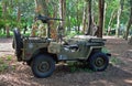 Second World War Jeep with machine Gun parked in woods with men dressed in uniforms in background.