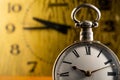 Silver antique pocket watch with Roman numerals and vintage table clock in blurry background. An old round white dial of Royalty Free Stock Photo