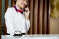 Silver bell on hotel reception service desk with blurred background of smiling Asian female receptionist talks to customer guest Royalty Free Stock Photo