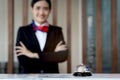 Silver bell on hotel reception service desk with blurred background of smiling beautiful female receptionist in black suit Royalty Free Stock Photo