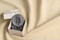 The silver bitcoin lies in a small orange gift box with a small bow on a blanket made of soft and fluffy light orange fleece Royalty Free Stock Photo