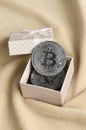 The silver bitcoin lies in a small orange gift box with a small bow on a blanket made of soft and fluffy light orange fleece Royalty Free Stock Photo