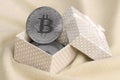 The silver bitcoin lies in a small orange gift box with a small bow on a blanket made of soft and fluffy light orange fleece Royalty Free Stock Photo