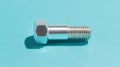 A silver bolt with a hexagonal head and threaded shaft is shown against a blue background. Royalty Free Stock Photo