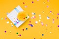 silver box decorated with a yellow flower made of thin fabric, yellow background strewn with confetti, copy space, top view Royalty Free Stock Photo