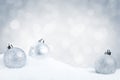 Silver Christmas baubles on snow with a silver background