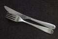 Silver chrome cutlery including a fork facing down and a knife facing inward, clean flatware set on dark grey table cloth