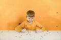 Silver coins are falling on the table to the child in an orange T-shirt