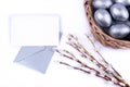 Silver colored Easter eggs in wicker basket, willow catkins branches, blank card on a silver envelope.