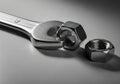 Silver-colored open-end wrench and two hexagonal nuts on a smooth, gray surface. The wrench, Royalty Free Stock Photo