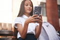 Silver colored smartphone in hands. School girl in uniform is outdoors near the building