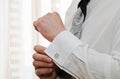 Silver cufflink that a man is putting on the cuff of his white shirt.