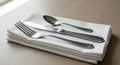 Silver cutlery set includes a fork, knife, and spoon placed on a neatly folded white Royalty Free Stock Photo