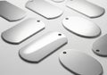 Silver dog tags are arranged on a light surface. The tags are made of metal, with a Royalty Free Stock Photo