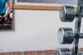 Some silver dumbbells are in the foreground and a mirror with the mirror image of an athlete hangs on the wall