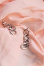 Silver earrings on an expensive pale pink silk background. Beautiful female jewelry. Chain earrings Royalty Free Stock Photo