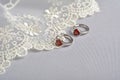 Silver earrings with red glass hearts with delicate ecru lace on a light gray background. space for text Royalty Free Stock Photo