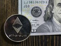 Silver Ethereum on US dollars. Digital currency close-up on a wooden background.Real coins of bitcoin on banknote of one hundred