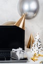 Silver festive box and blank screen laptop with party hats and balloons. Royalty Free Stock Photo