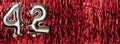 Silver foil balloon number 42 on a background of red tinsel decoration. Birthday greeting card, inscription forty-two