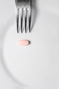 Silver fork and pink pill on the white plate, a Royalty Free Stock Photo