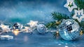 Silver glass ball, jingle bells and glowing star lights garland. green christmas tree branch on blurred blue background Royalty Free Stock Photo