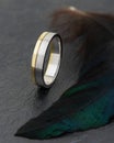Silver and gold combined ring on black background with green feathe