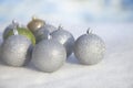 Silver, green and gold Christmas baubles in snow