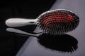 Silver hairbrush with red middle and high-quality multilayer teeth on reflective black background. subject photo. individual