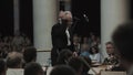 Silver-haired kapellmeister conducting violin orchestra in classic concert hall