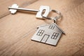 Close up silver home shaped keychain with key on wooden background. Mortgage, investment, real estate, property and new home conce