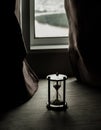 Silver hourglass or Sandglass is placed on a glass windowsill of the room