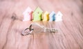 Silver Keychain laying on wooden Surface in front of miniature symbol of various coloured houses