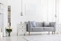 Silver lamps above white cabinets in apartment interior with flowers and grey settee. Real photo