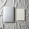 Silver laptop and white notebook placed side-by-side on a textured gray fabric. The Royalty Free Stock Photo