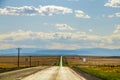 Silver line of two lane highway stretches to horizon with blue layered mountains in the distance and dry fields  and electric Royalty Free Stock Photo