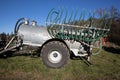 Silver manure wagon without tractor with green hoses standing on an autumn meadow in the morning, sunshine without clouds Royalty Free Stock Photo